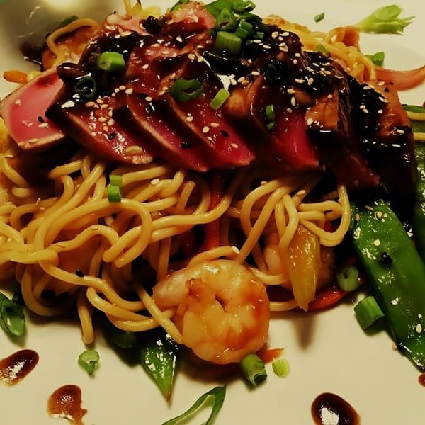 Seared tuna with sesame seeds, noodles, shrimp, and snap peas on a white plate.