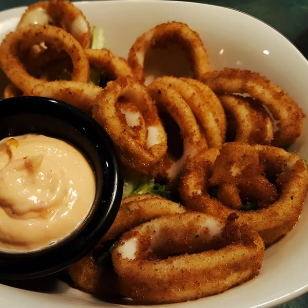 A white bowl filled with golden-brown fried calamari rings and a side of creamy dipping sauce.
