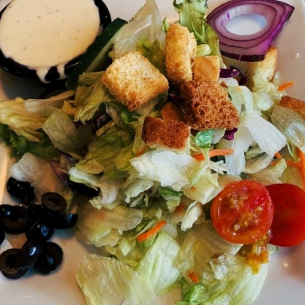 A fresh side salad with lettuce, croutons, tomatoes, olives, red onion, and ranch dressing.
